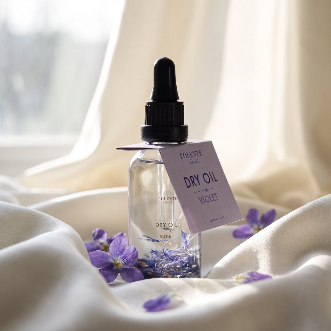 Violet Dry Oil 50 ml çok amaçlı kuru yağ — fildişi ipek kıvrımları üzerinde taze menekşelerle konsept görseli
