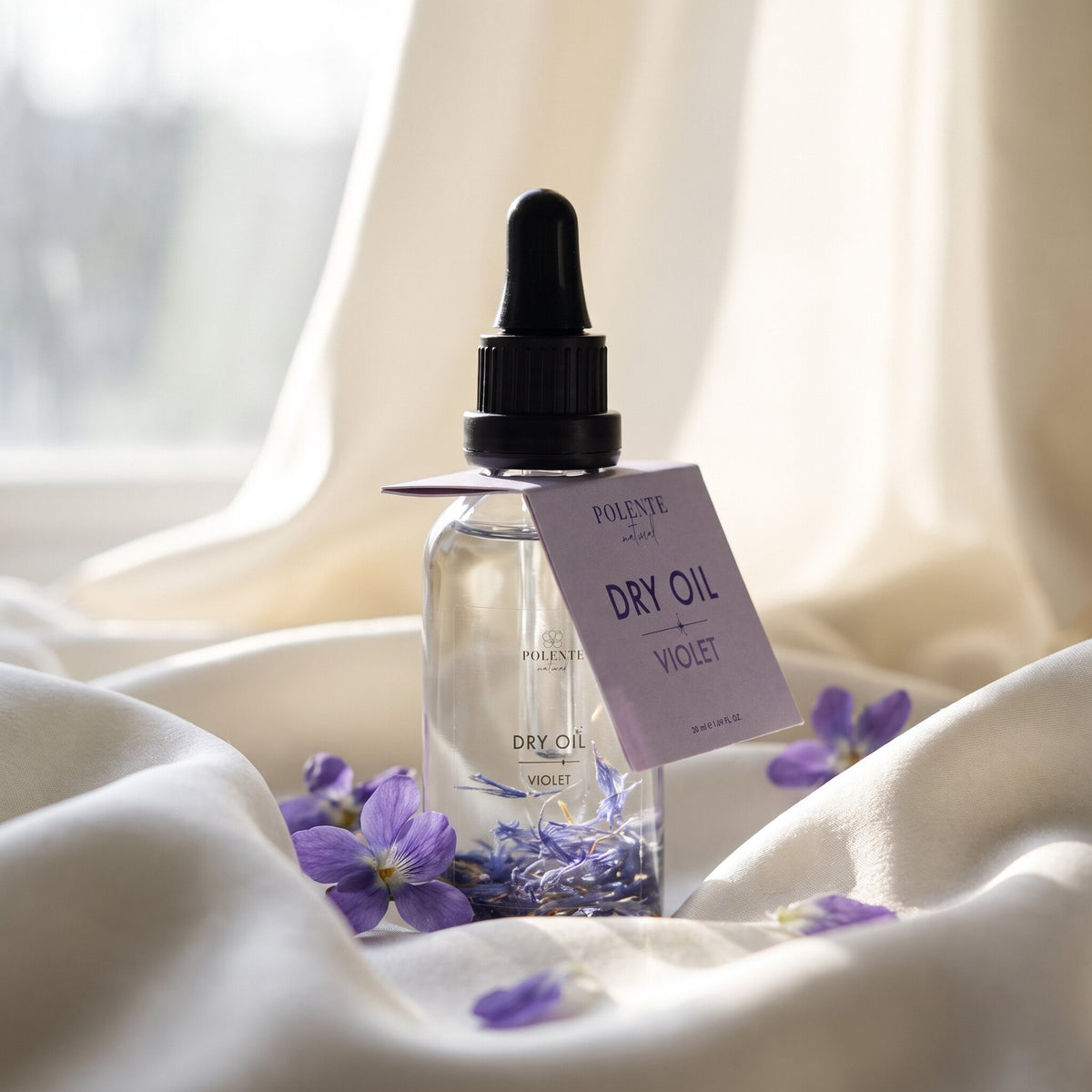 Violet Dry Oil 50 ml çok amaçlı kuru yağ — fildişi ipek kıvrımları üzerinde taze menekşelerle konsept görseli