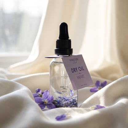 Violet Dry Oil 50 ml çok amaçlı kuru yağ — fildişi ipek kıvrımları üzerinde taze menekşelerle konsept görseli