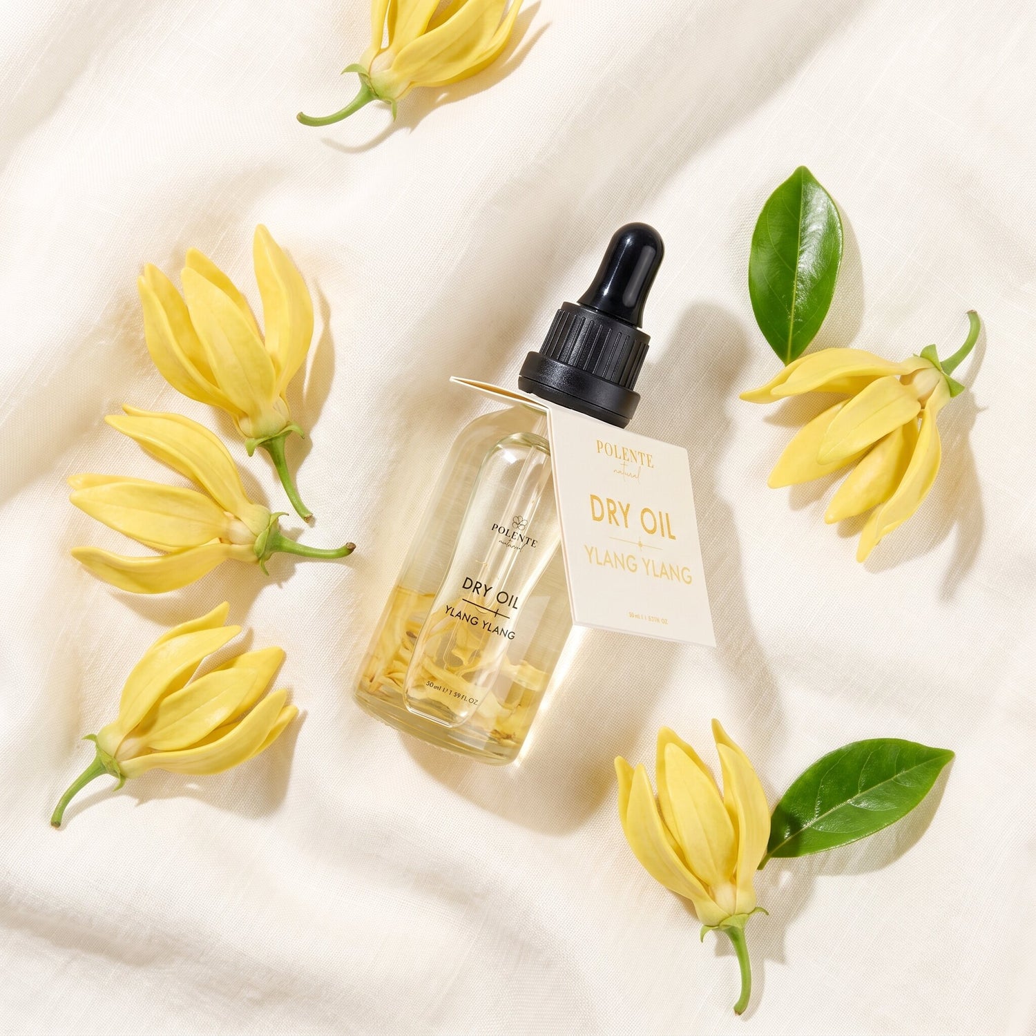 Ylang Ylang Dry Oil 50 ml çok amaçlı kuru yağ — krem keten üzerinde ylang ylang çiçekleriyle ferah konsept görseli